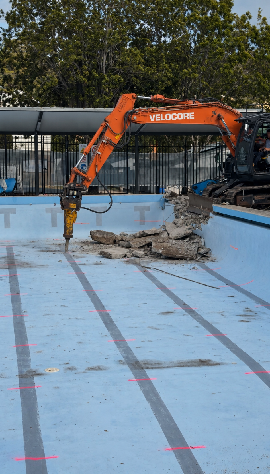 Excavator using a hydraulic breaker to remove concrete inside an empty pool